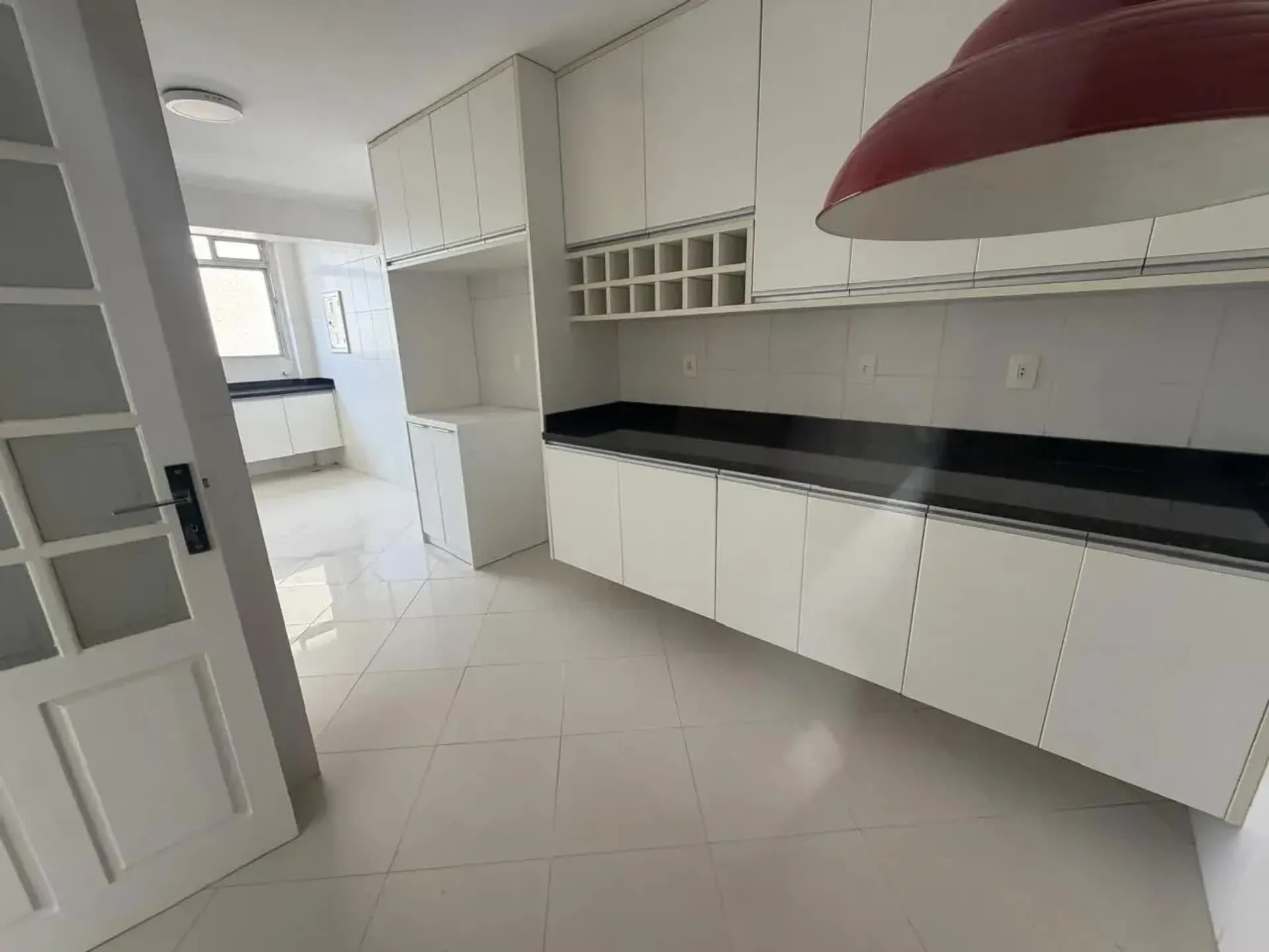 Cozinha planejada branca com bancada de granito preto, cuba dupla e coifa.