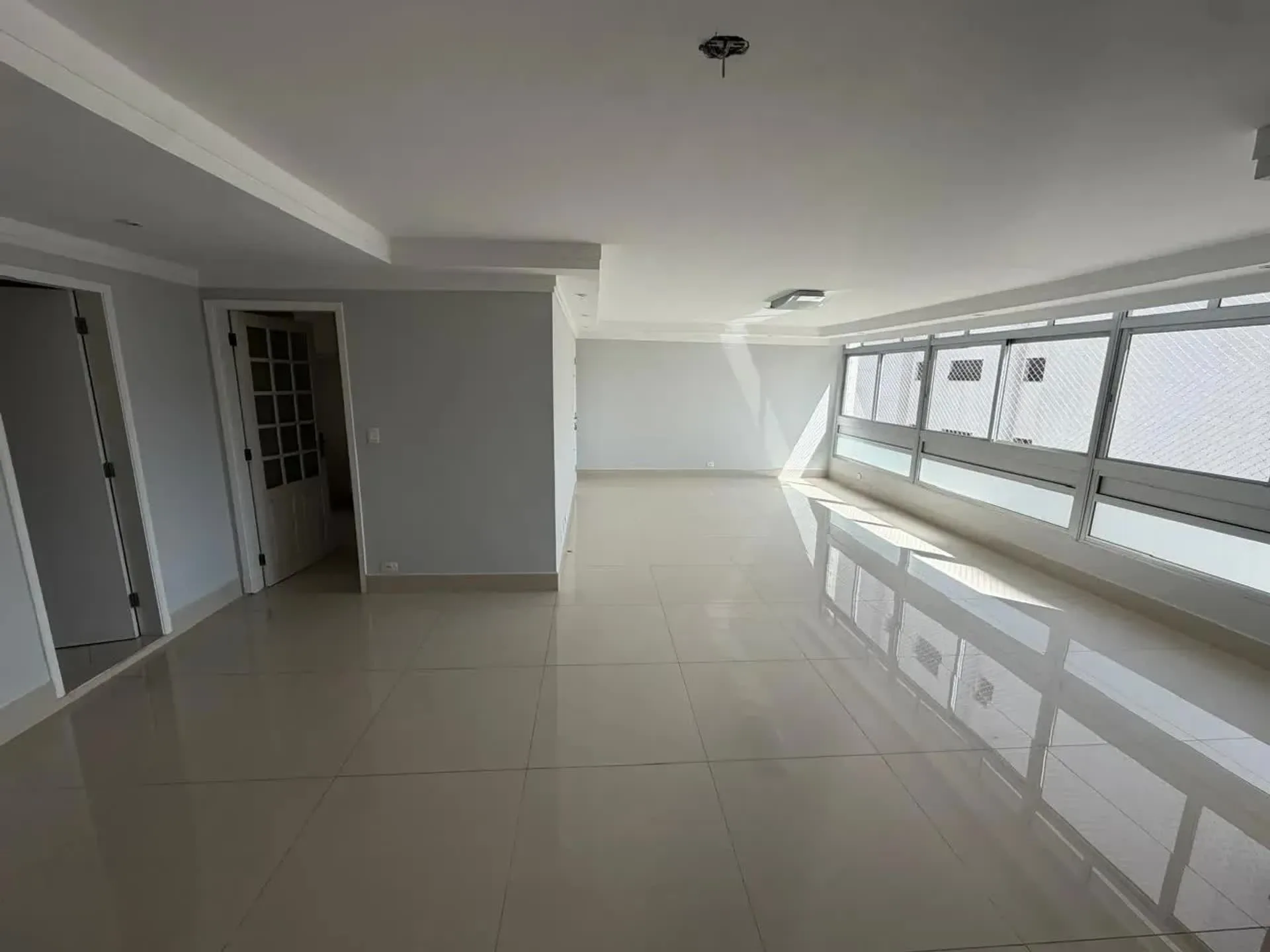 Living amplo e vazio do apartamento da Rua Caconde, com piso claro e janelas em toda a fachada social.