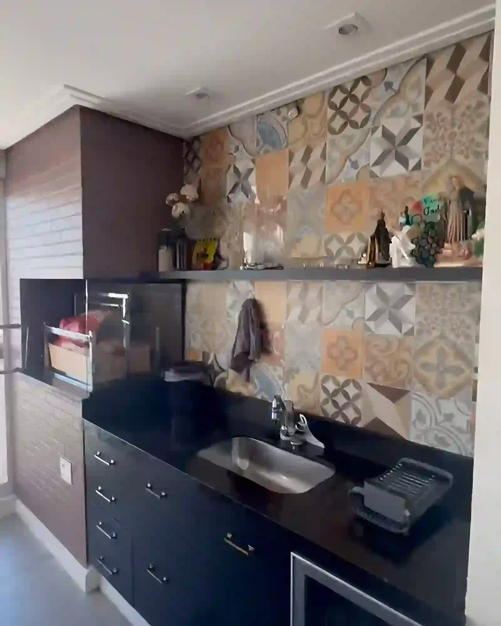 Churrasqueira de alvenaria em tijolo aparente do piso ao teto, com grelha de altura regulável e ladrilho hidráulico patchwork ao lado.